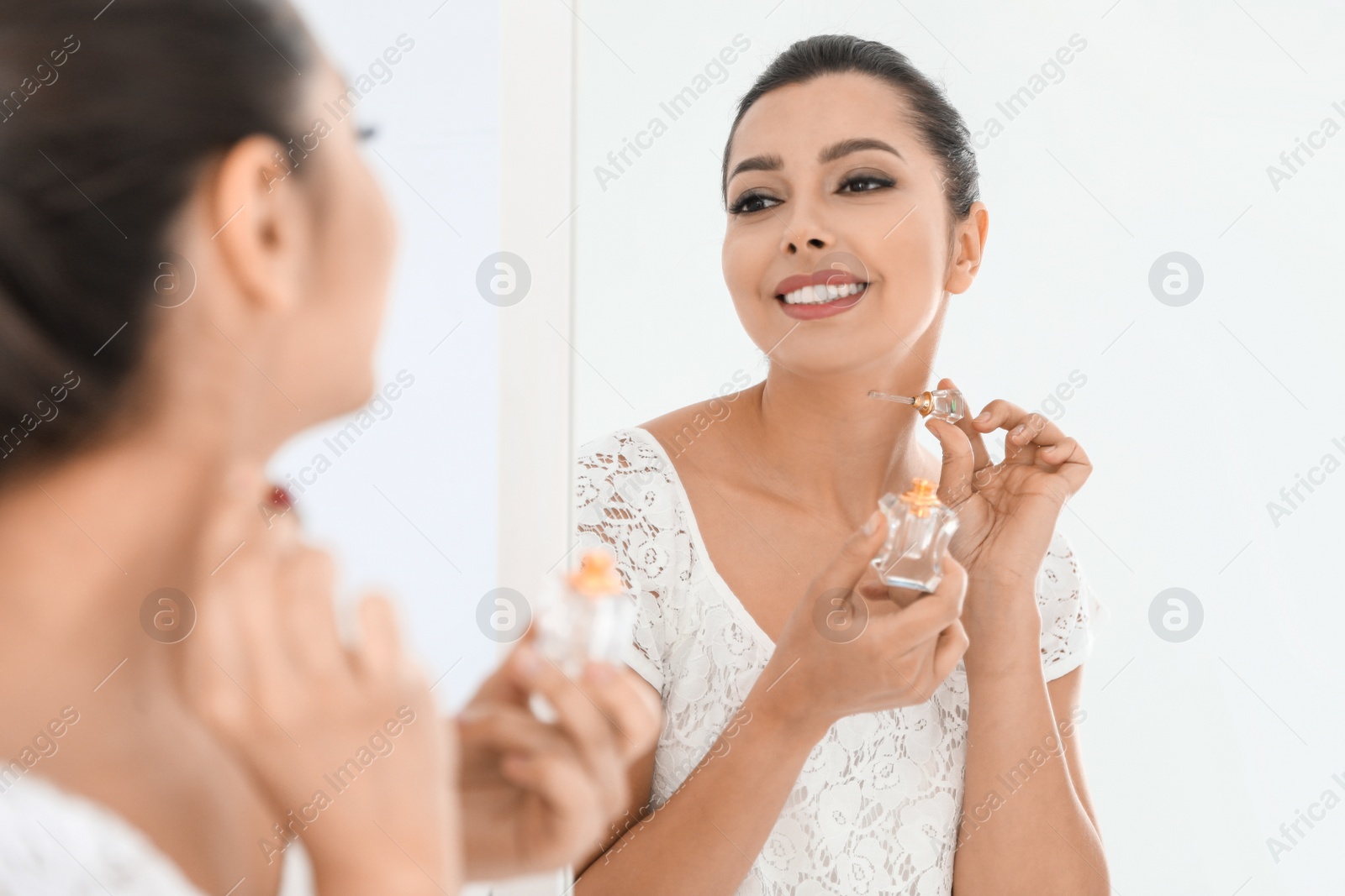 Photo of Young woman with bottle of perfume near mirror indoors