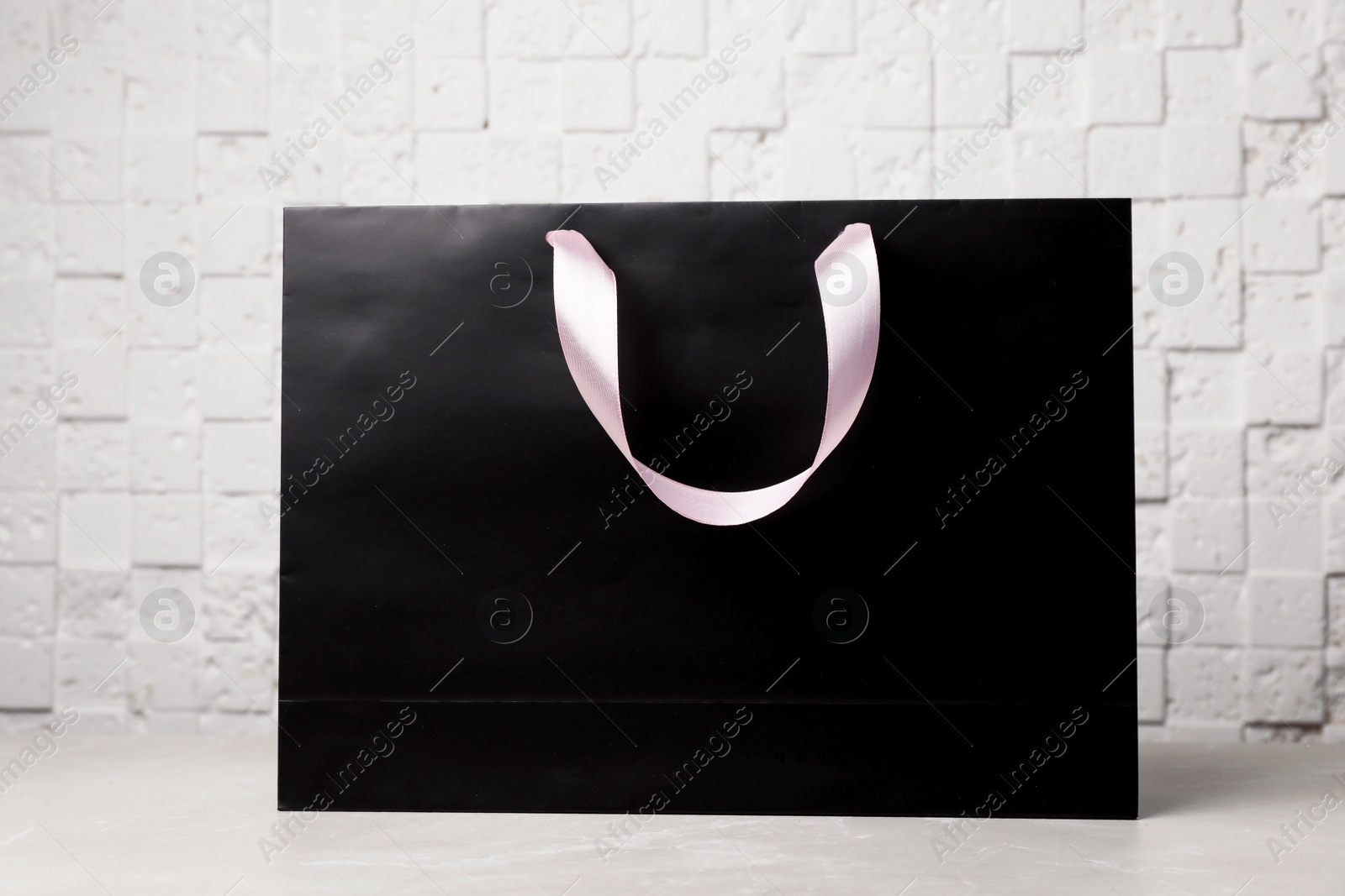 Photo of Paper shopping bag with ribbon handles on table near white wall. Mockup for design