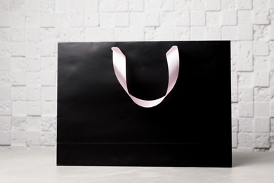 Paper shopping bag with ribbon handles on table near white wall. Mockup for design