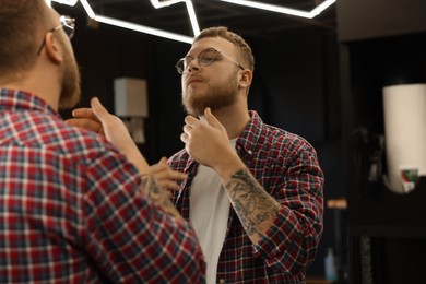 Young bearded man near mirror in barbershop