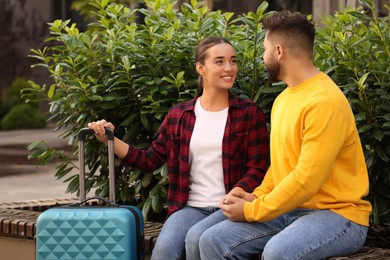 Long-distance relationship. Beautiful happy couple on bench and suitcase outdoors