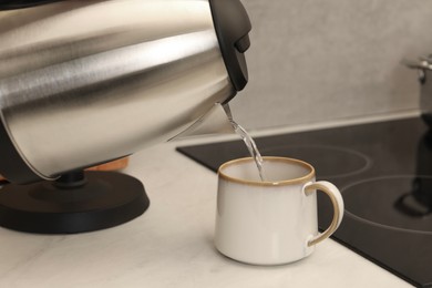 Photo of Pouring hot water from electric kettle into cup in kitchen, closeup