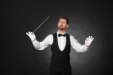 Professional conductor with baton on black background