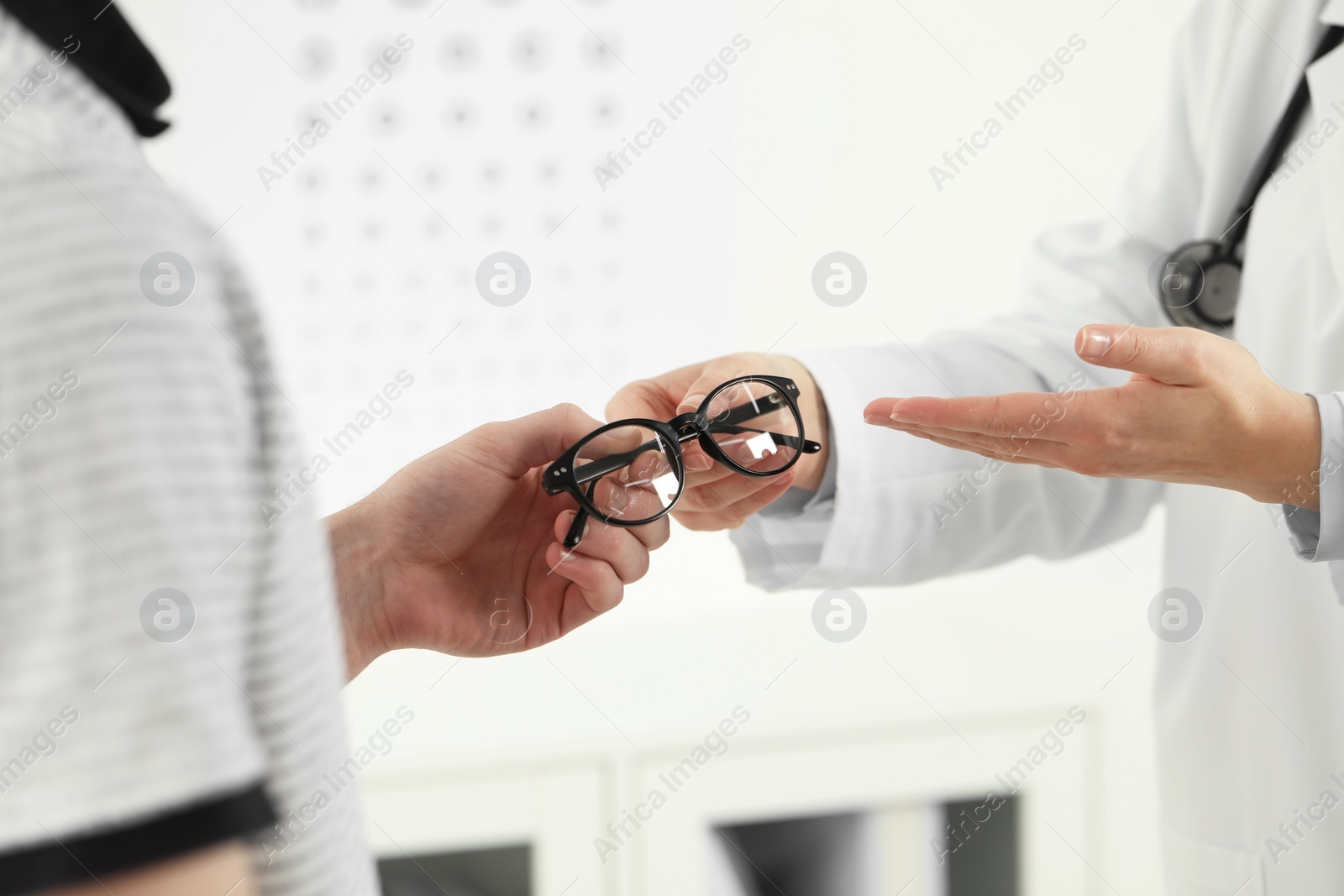 Photo of Vision testing. Ophthalmologist giving glasses to young man indoors, closeup