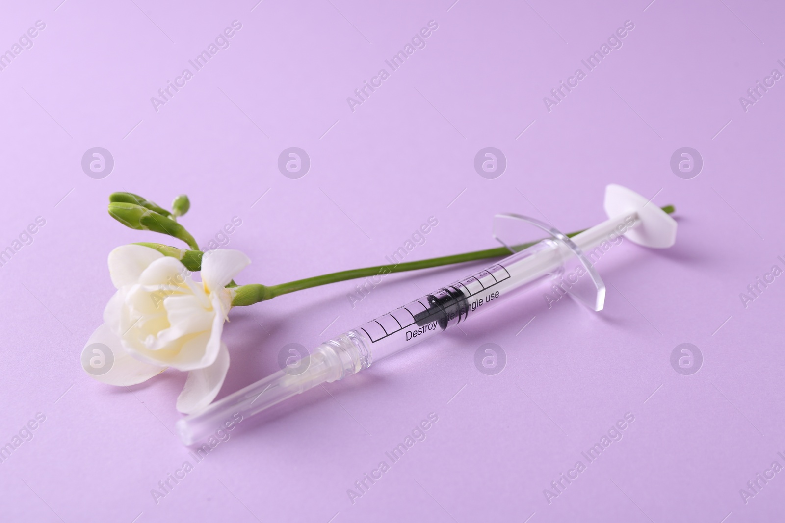 Photo of Cosmetology. Medical syringe and freesia flower on violet background