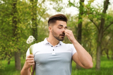 Young man with dandelions suffering from seasonal allergy outdoors