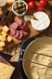 Photo of Fondue with tasty melted cheese, forks and different snacks on table, top view