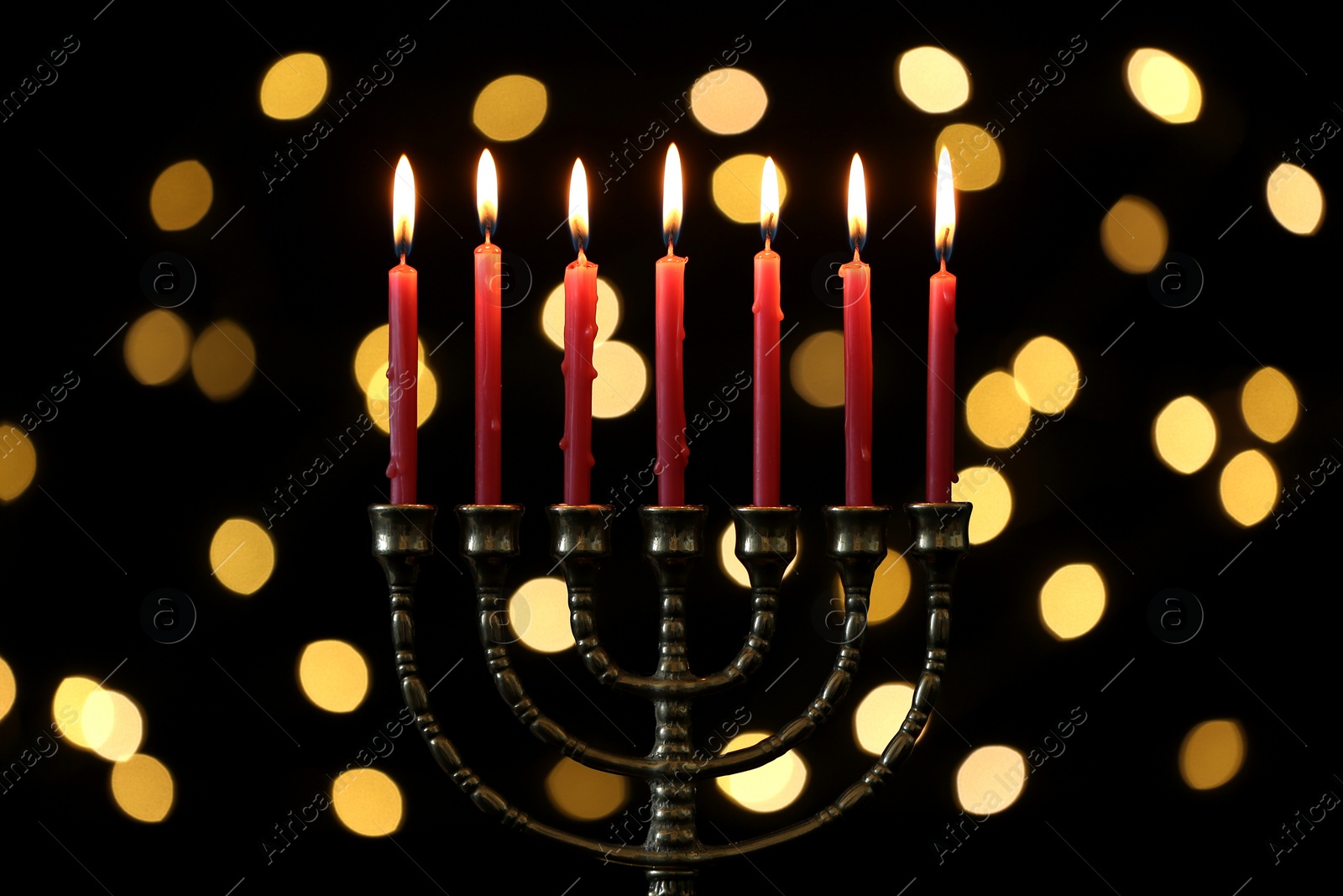 Photo of Golden menorah with burning candles against dark background and blurred festive lights