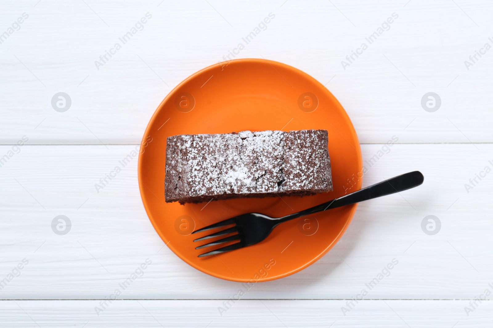 Photo of Piece of tasty chocolate sponge cake with powdered sugar on white wooden table, top view