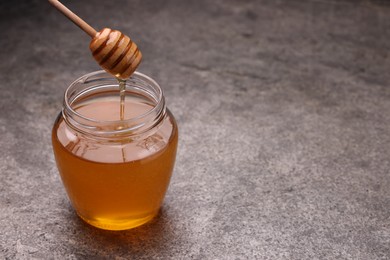 Photo of Pouring sweet golden honey from dipper into jar at grey textured table, space for text