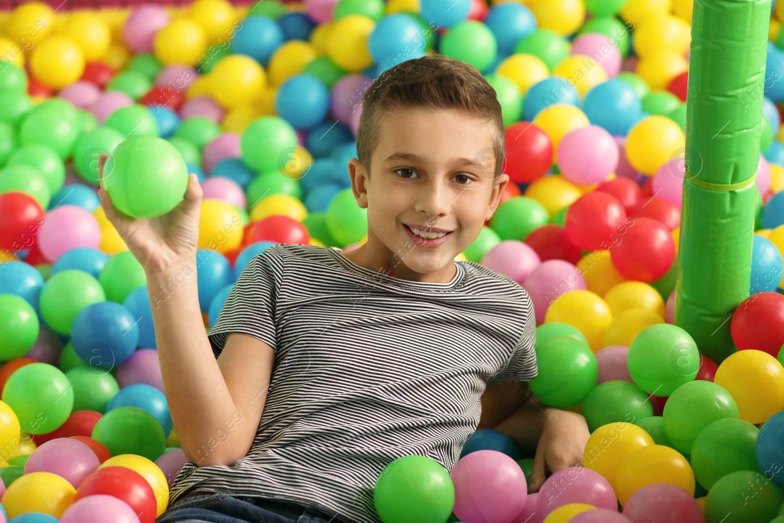 Photo of Cute little child playing in ball pit at indoor amusement park