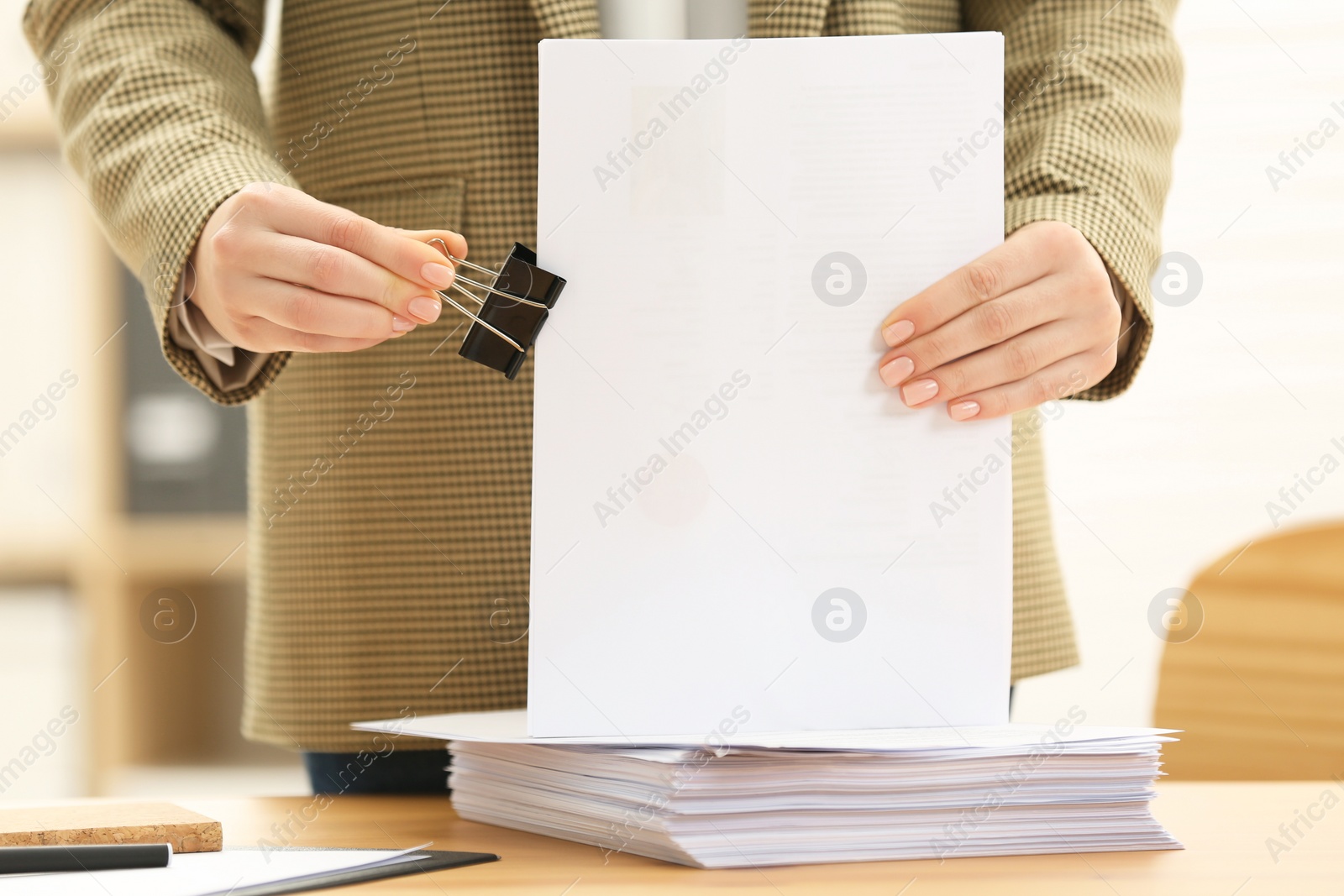 Photo of Woman attaching documents with metal binder clip at table in office, closeup
