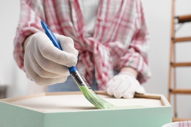 Photo of Woman painting honeycomb shaped shelf with brush indoors, closeup