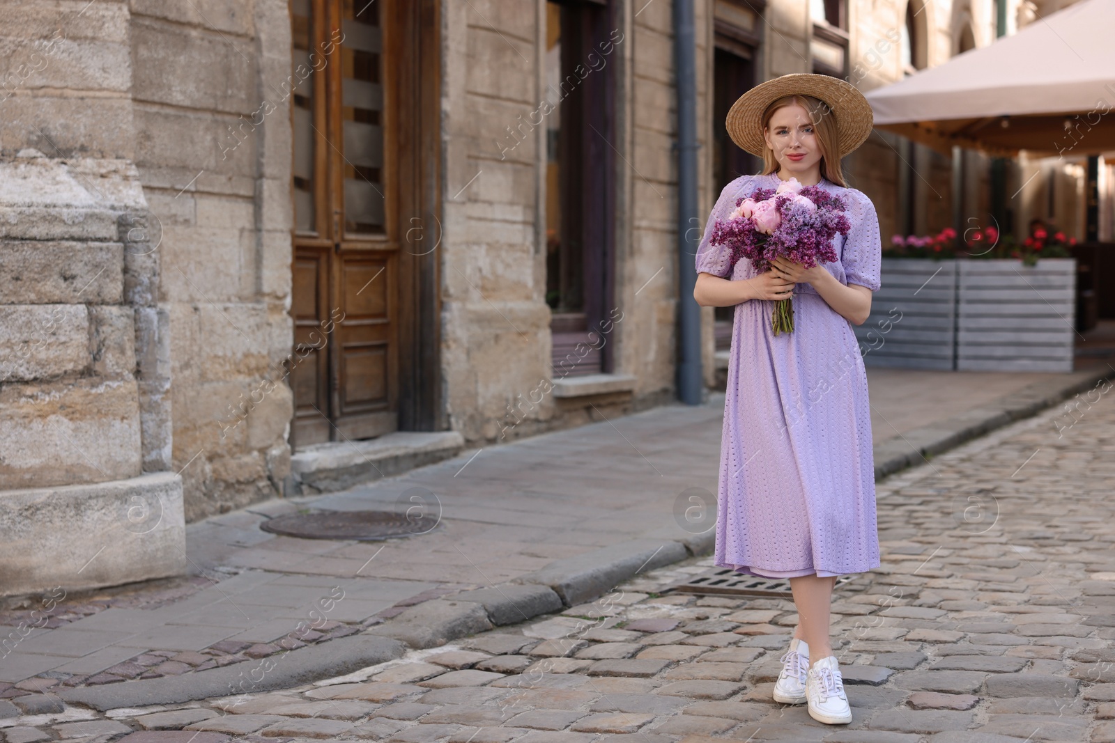 Photo of Beautiful woman with bouquet of spring flowers on city street, space for text