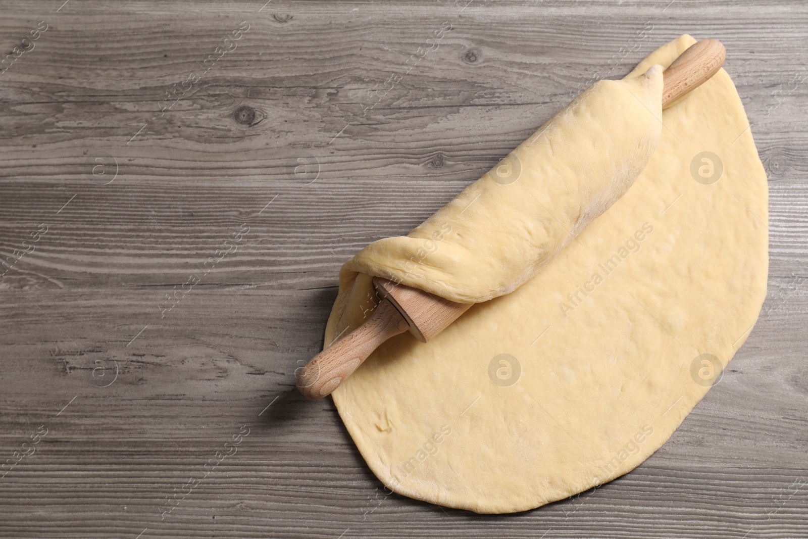 Photo of Raw dough and rolling pin on wooden table, top view. Space for text