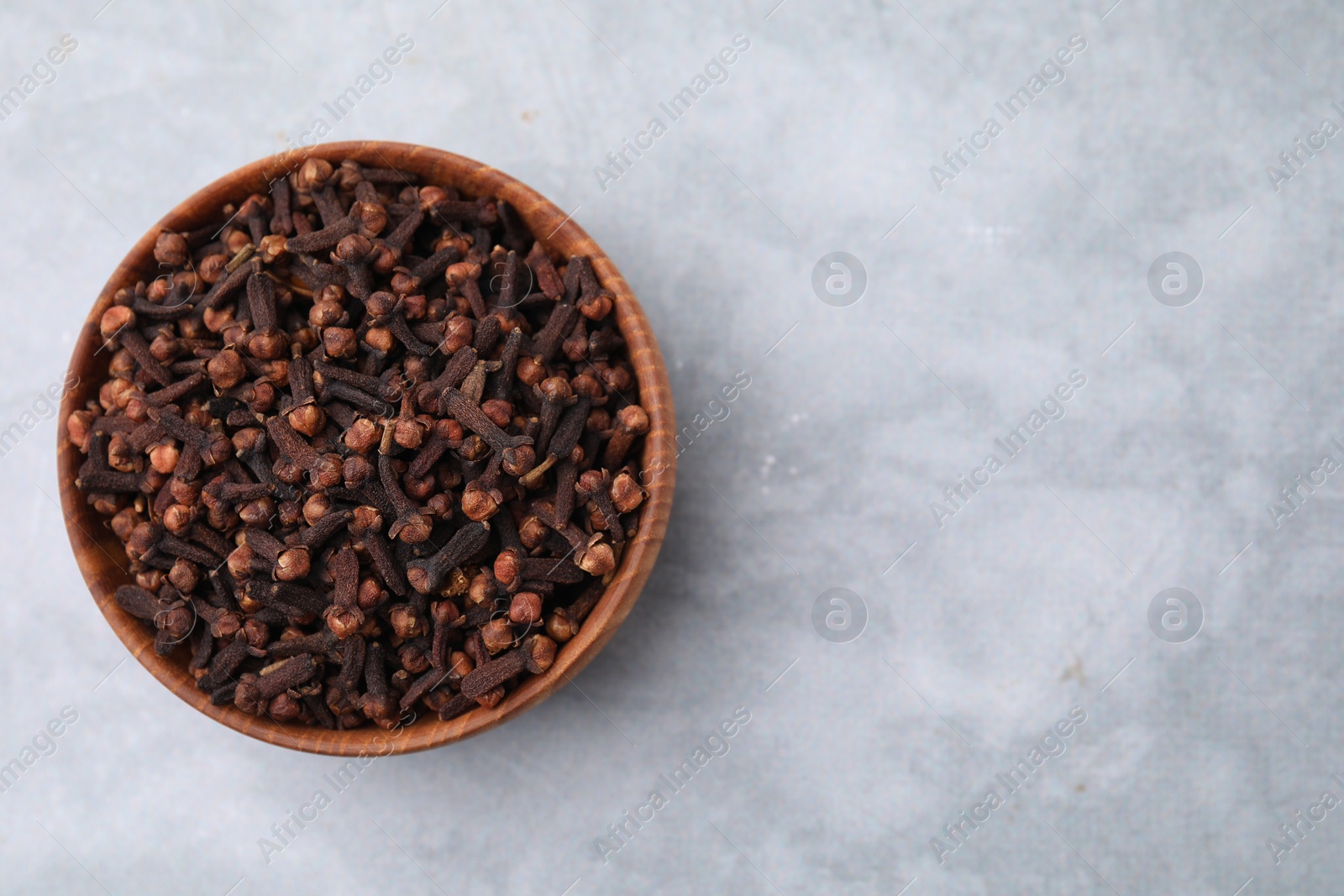 Photo of Aromatic cloves in bowl on gray table, top view. Space for text