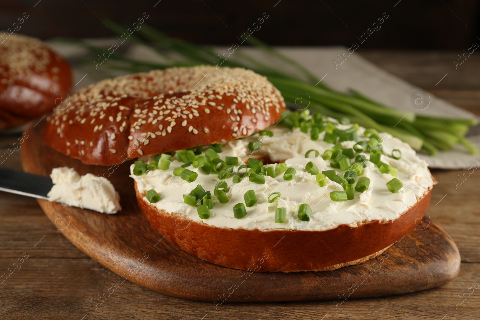 Photo of Delicious bagel with cream cheese and green onion on wooden table, closeup
