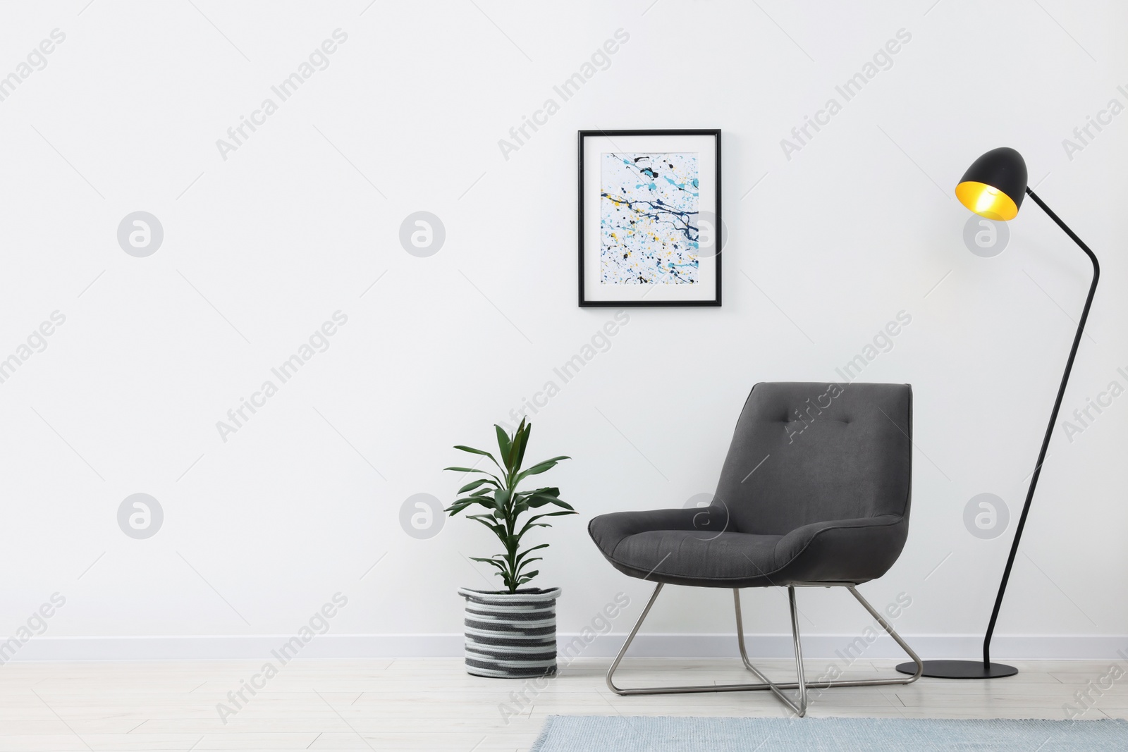 Photo of Stylish living room interior with comfortable armchair, houseplant and lamp near white wall indoors. Space for text
