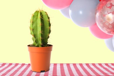 Image of Balloons over table with cactus against pastel yellow background