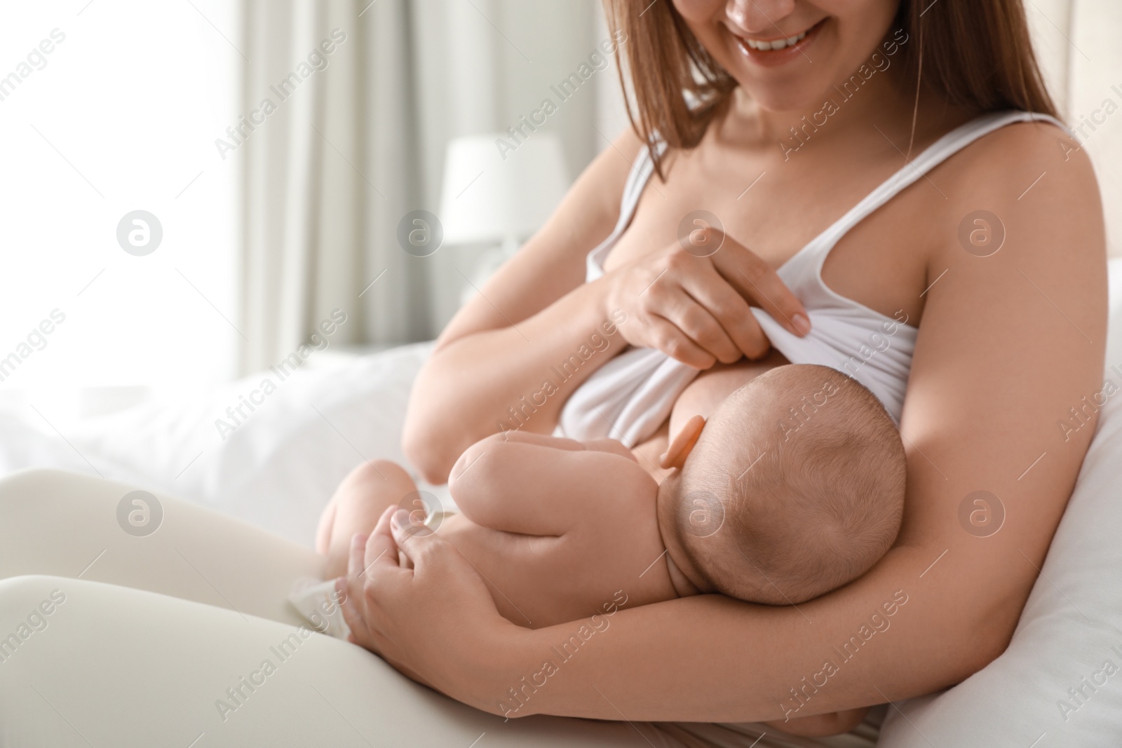 Photo of Young woman breastfeeding her little baby on bed at home, closeup