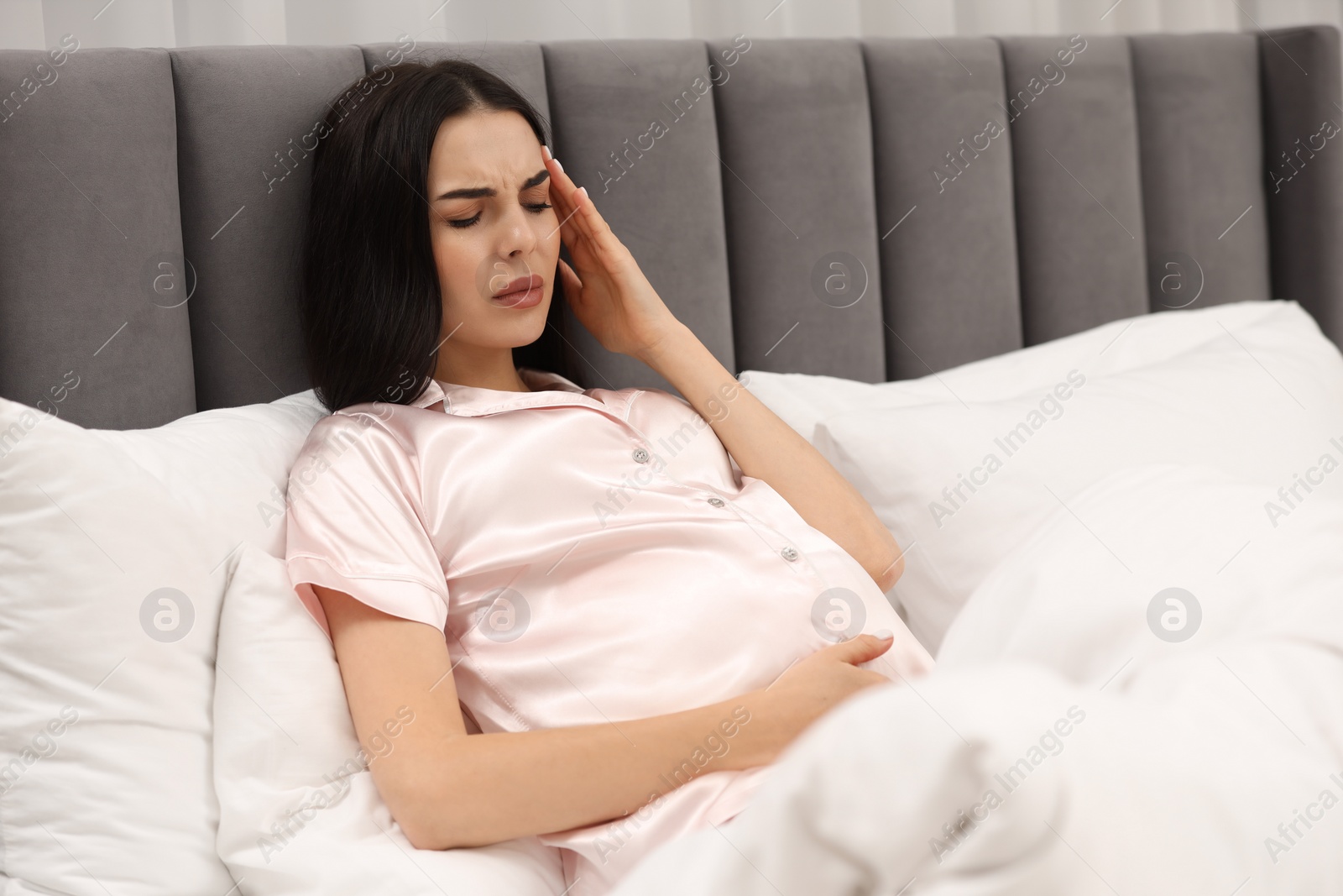 Photo of Pregnant woman suffering from headache in bed at home