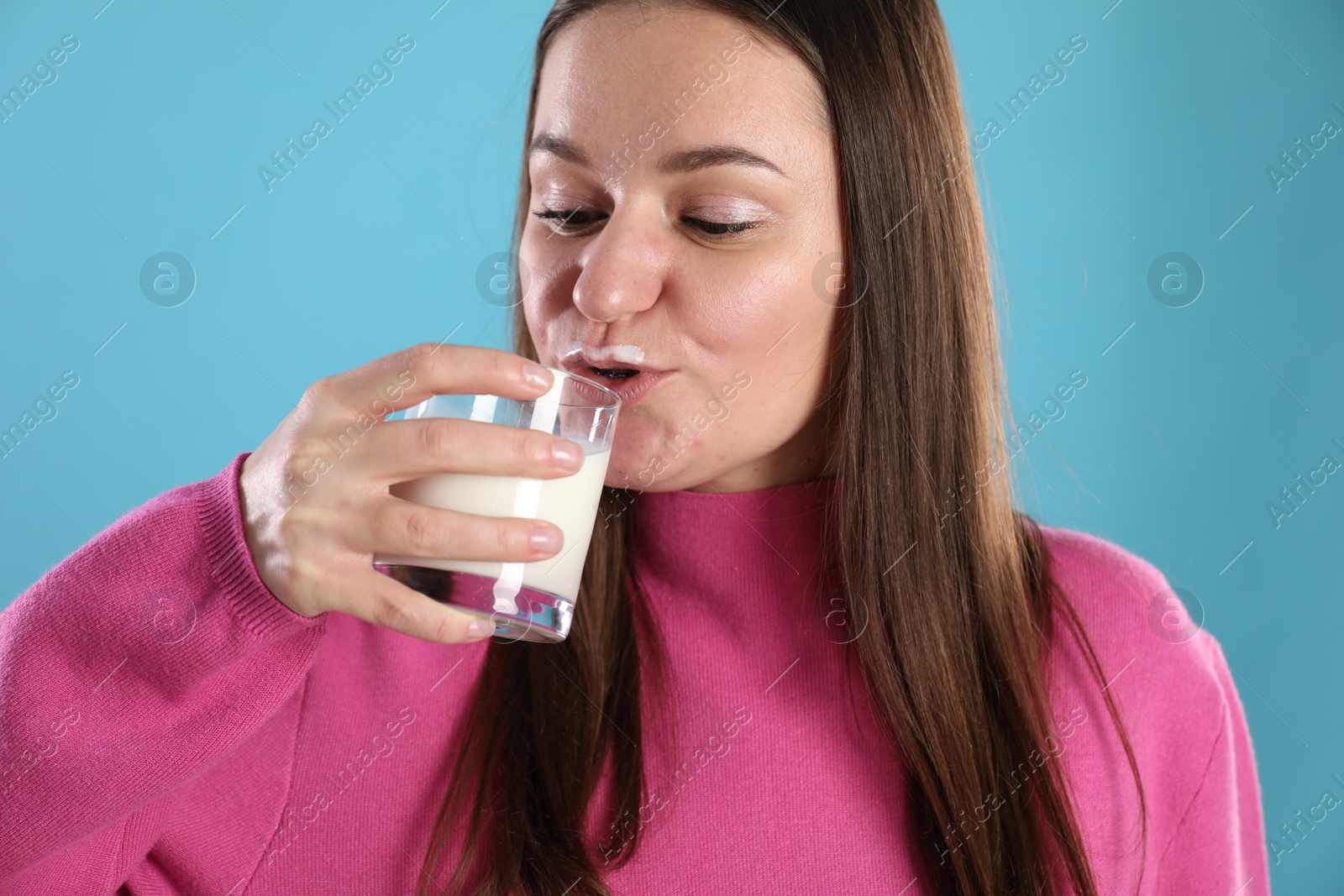 Photo of Happy woman with milk mustache holding glass of drink on light blue background