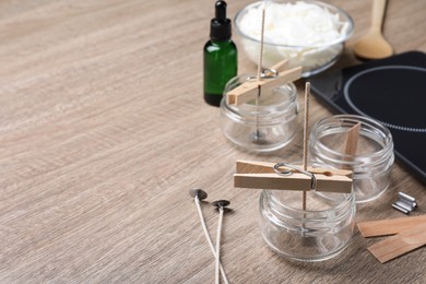 Photo of Glass jars with wicks and clothespins as stabilizers on wooden table, space for text. Making homemade candles
