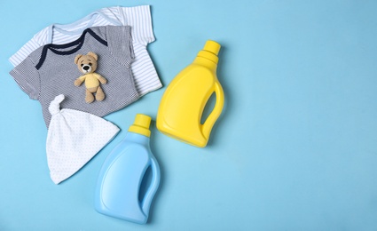 Photo of Flat lay composition with bottles of detergent and children's clothes on light blue background. Space for text