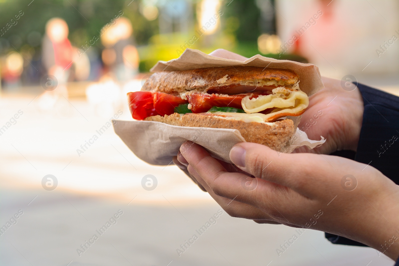 Photo of Woman holding tasty sandwich with vegetables outdoors, closeup and space for text. Street food