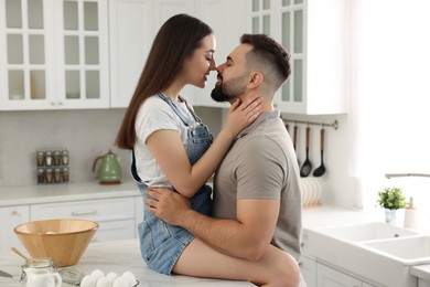 Photo of Affectionate young couple kissing in light kitchen