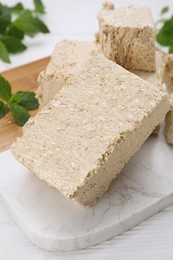 Pieces of tasty halva and mint on white table, closeup