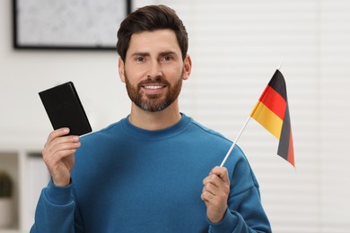 Immigration. Happy man with passport and flag of Germany indoors