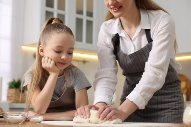 Making bread. Mother and her daughter kneading dough at wooden table in kitchen