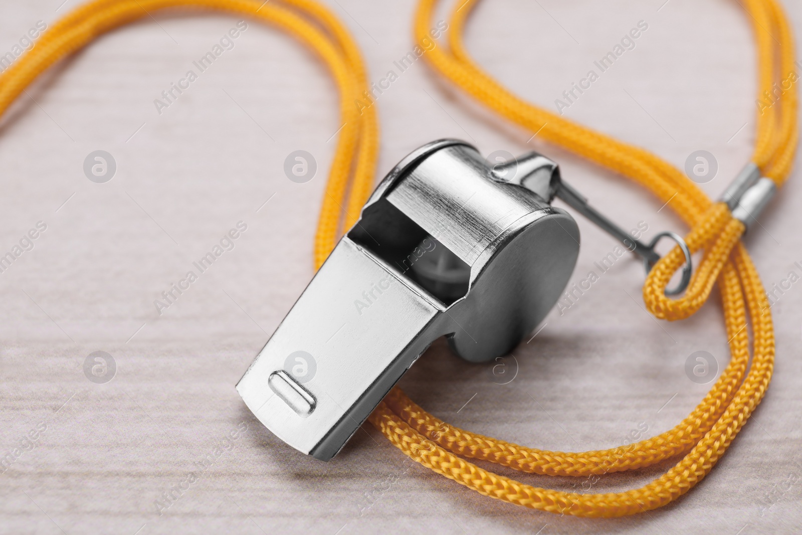 Photo of One metal whistle with cord on light wooden table, closeup