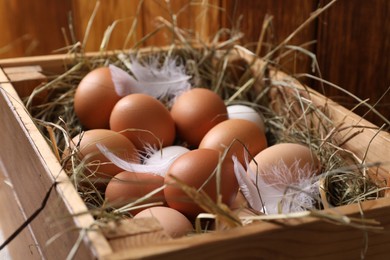 Photo of Fresh chicken eggs and dried hay in wooden crate, closeup