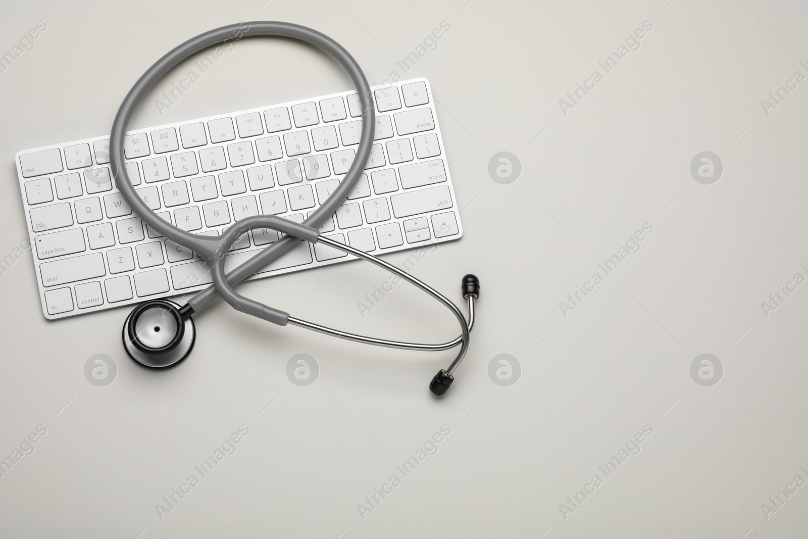 Photo of Keyboard and stethoscope on beige background, flat lay. Space for text