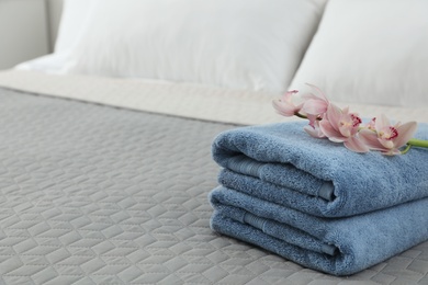 Stack of clean towels with flowers on bed. Space for text