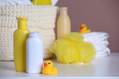 Bottles of baby cosmetic products and rubber duck on white table. Space for text