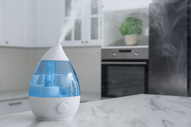 Photo of Modern air humidifier on marble table in kitchen. Space for text