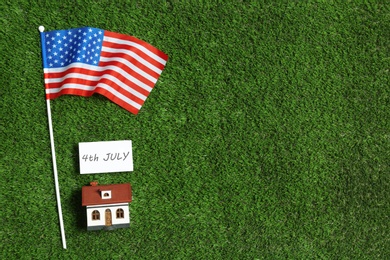 Photo of Flat lay composition with house model, USA flag and card on green grass, space for text. Happy Independence Day