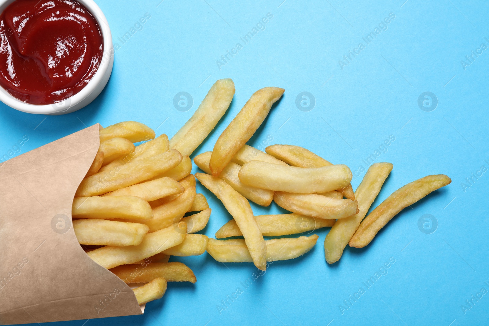 Photo of Paper cup with French fries and ketchup on light blue table, above view