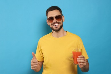 Photo of Man holding glass of delicious juice on light blue background