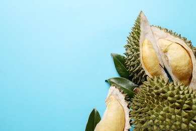 Photo of Fresh ripe durians and leaves on light blue background, flat lay. Space for text