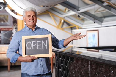 Photo of Senior business owner holding OPEN sign in his restaurant