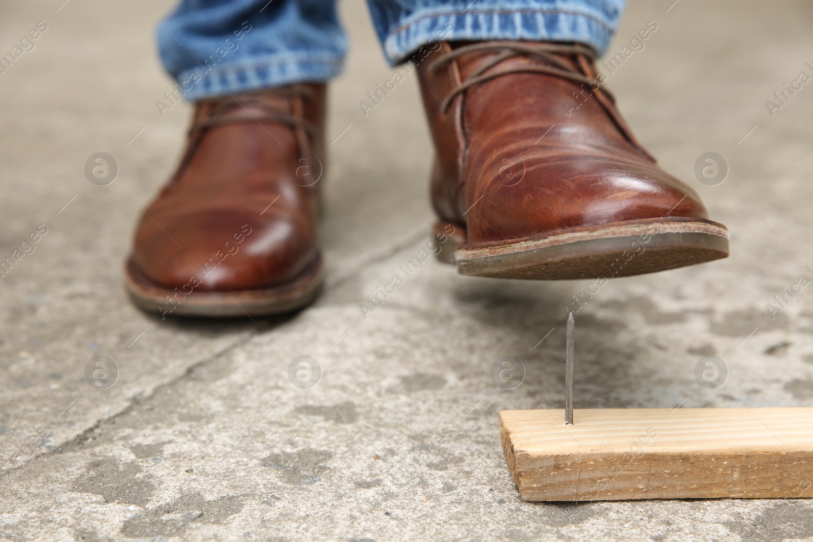 Photo of Careless man stepping on nail in wooden plank outdoors, closeup