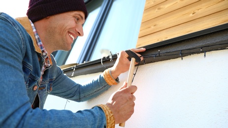 Photo of Man decorating house with Christmas lights outdoors