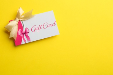 Gift card with bow on yellow background, top view. Space for text