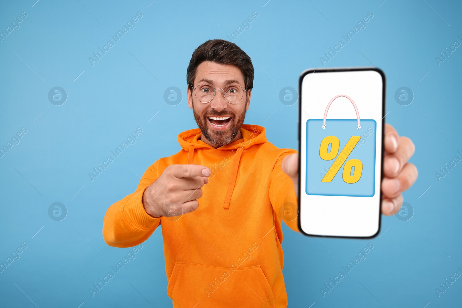 Image of Discount, offer, sale. Man pointing at mobile phone with illustration of bag and percent sign on screen, light blue background