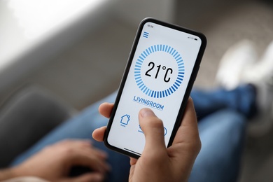 Image of Man using smartphone to control heating system in house, closeup