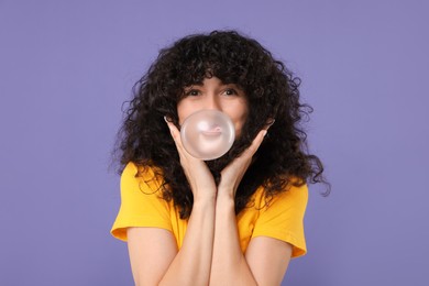 Photo of Beautiful young woman blowing bubble gum on purple background